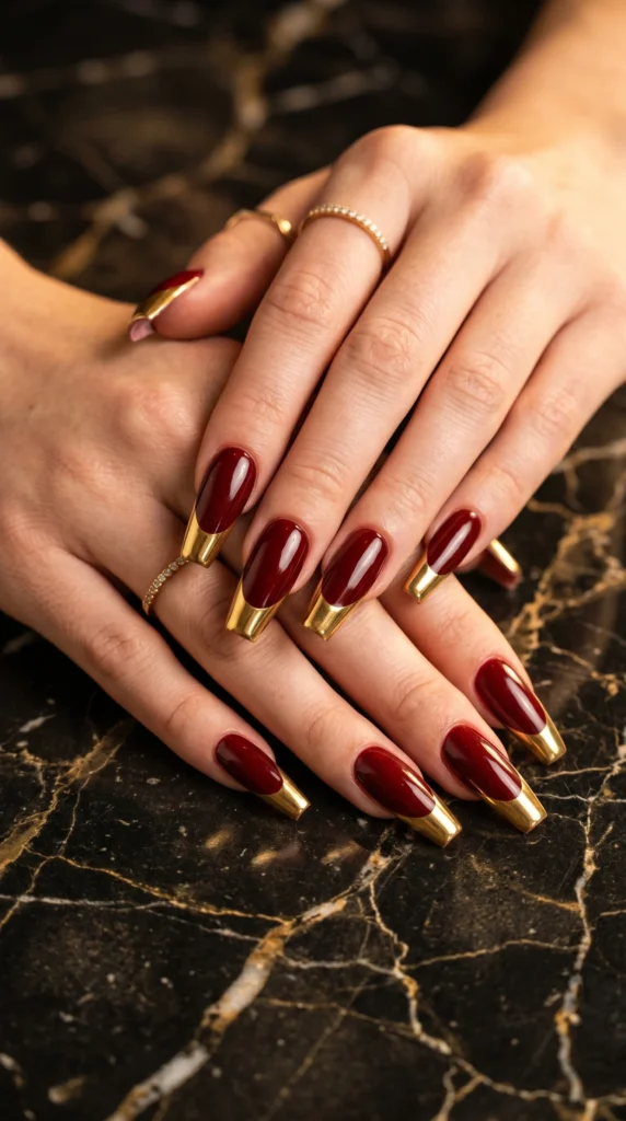 Long coffin nails in oxblood red with gold chrome mirror tips for powerful elegant expensive statement