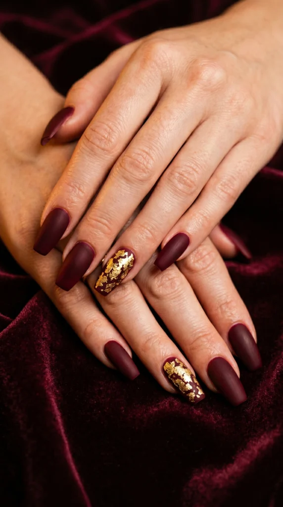 Coffin nails in deep burgundy velvet matte with gold leaf flake accent nails for rich luxurious look