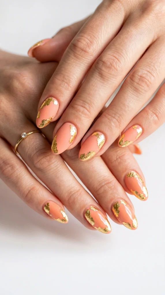 Almond nails in matte soft coral with organic gold leaf patches, summer editorial nail art style