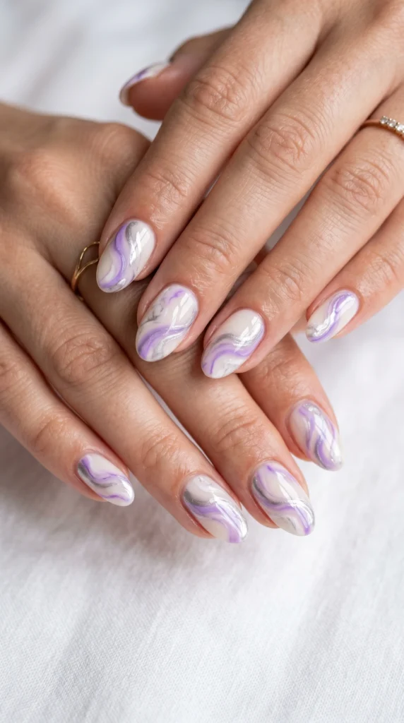 Oval nails with cream base and flowing lilac and silver swirl marble effect — each nail unique