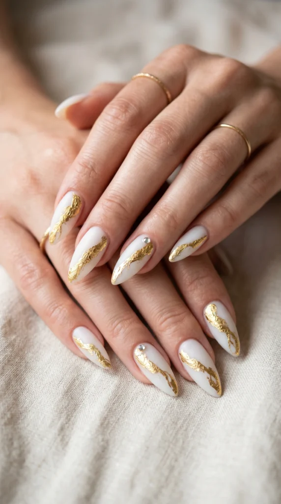 Stiletto nails in milky white with diagonal gold foil crinkle veining and rhinestone accent