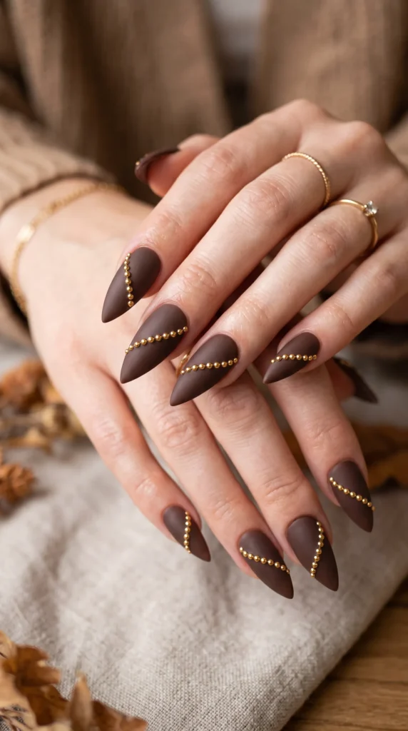 A woman with brown nail polish and gold studs on her nails.