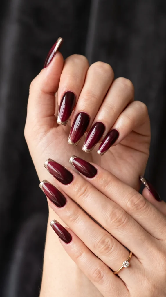 A hand with red nail polish and a gold stripe.