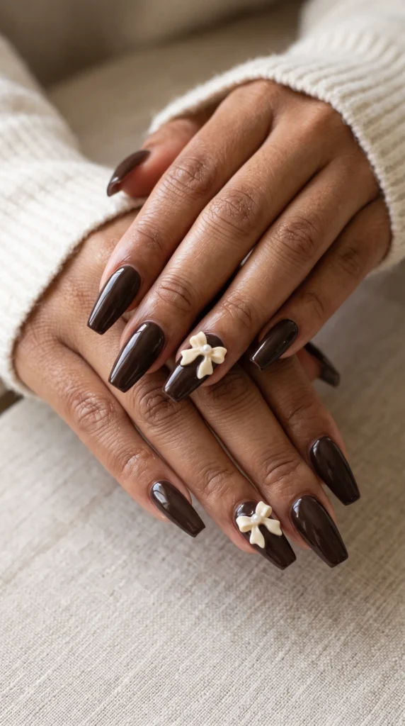 A woman with brown nails and a white bow on her nails.
